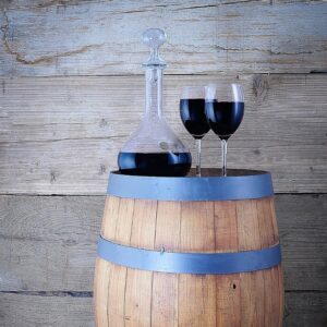 Un decantador de cristal con vino tinto y dos copas sobre un barril de madera rústico.