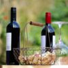 Botellas de vino tinto de uva Garnacha, copa vacía y cesta con corchos en un entorno natural.