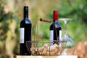 Botellas de vino tinto de uva Garnacha, copa vacía y cesta con corchos en un entorno natural.