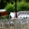 Servido de vino espumoso efervescente desde una botella verde en una fila de copas de flauta al aire libre, perfecto para ilustrar un brindis grupal con Cava o Corpinnat.