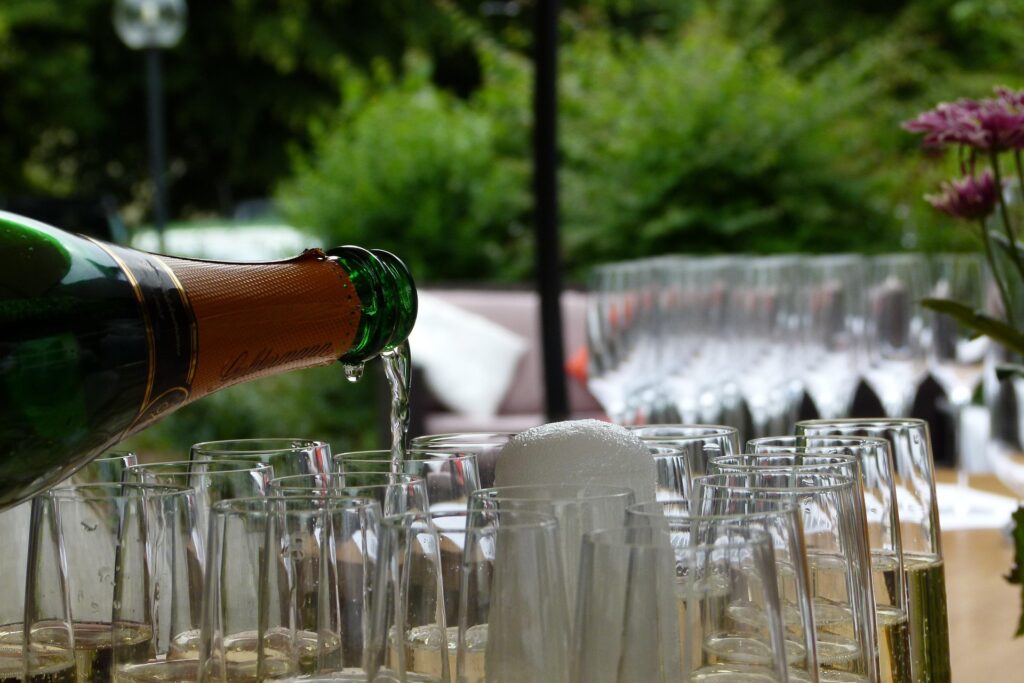 Servido de vino espumoso efervescente desde una botella verde en una fila de copas de flauta al aire libre, perfecto para ilustrar un brindis grupal con Cava o Corpinnat.
