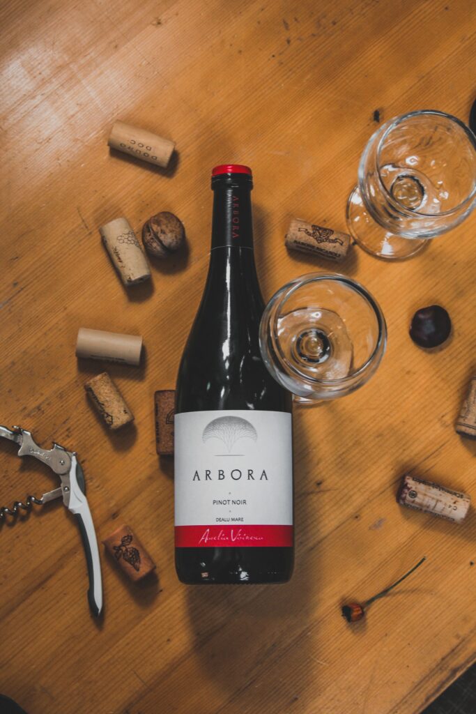 Botella de vino sobre una mesa de madera rodeada de varios tipos de corcho, un sacacorchos y copas vacías.