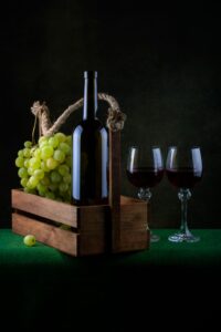 Bodegón elegante con botella de vino, uvas frescas y dos copas de tinto que ilustra la diferencia entre vinos monovarietales vs coupage.