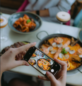 Persona tomando una foto con el móvil a una paella de marisco en un restaurante