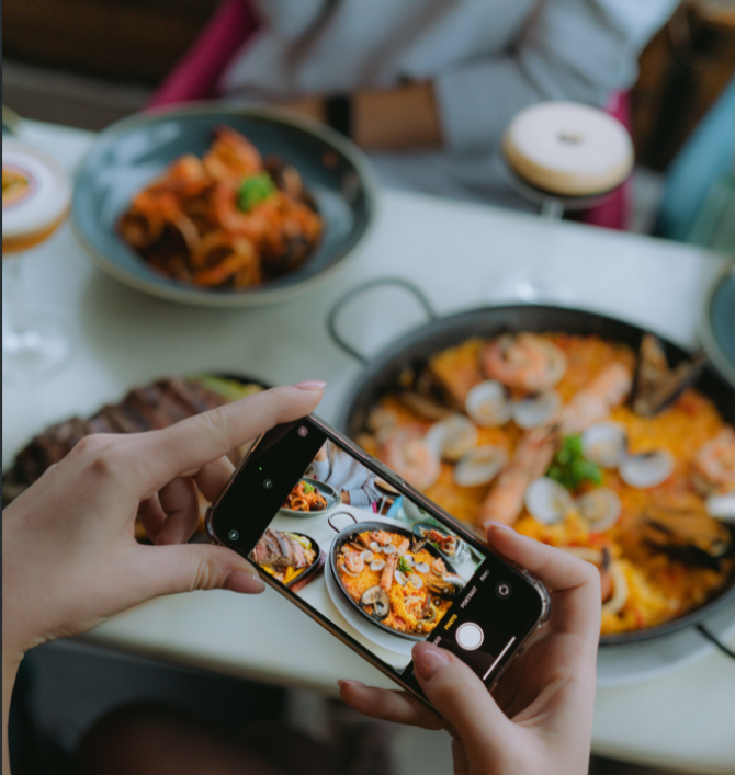 Persona tomando una foto con el móvil a una paella de marisco en un restaurante